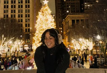 Photo of engagement staff member Adriana, posing for a photo in a park with a Christmas tree and lights in the background.