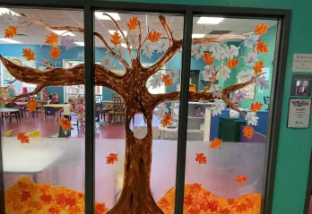 A tree is painted on the windows of KidZone at the Betty J. Pullum Y, with paper leaves decorated by the children.