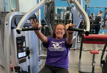 Jackie, a member of the Betty J. Pullum Y, smiles for a photo while she works out at a weight machine.