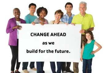 A group of smiling people stand with a sign that reads "Change ahead as we build for the future".