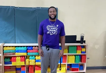 Christian smiles for a photo in the gym as he prepares the area for after school care.