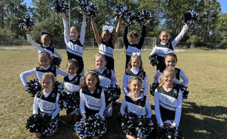 A youth cheer team takes a group photo together on the field at the Betty J. Pullum YMCA.