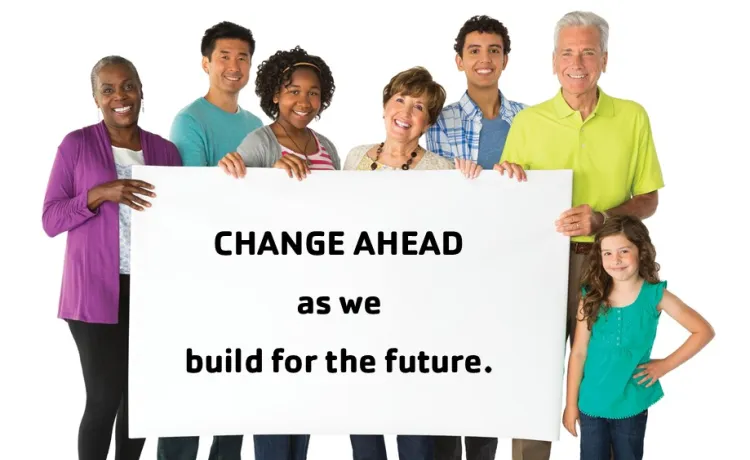 A group of smiling people stand with a sign that reads "Change ahead as we build for the future".