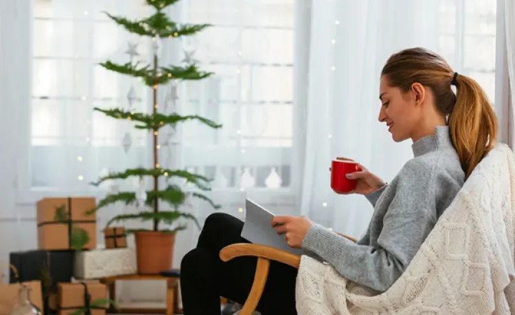 A woman is pictured enjoying a quiet moment in a living room decorated for Christmas, as she holds a mug in one hand and reads a book.