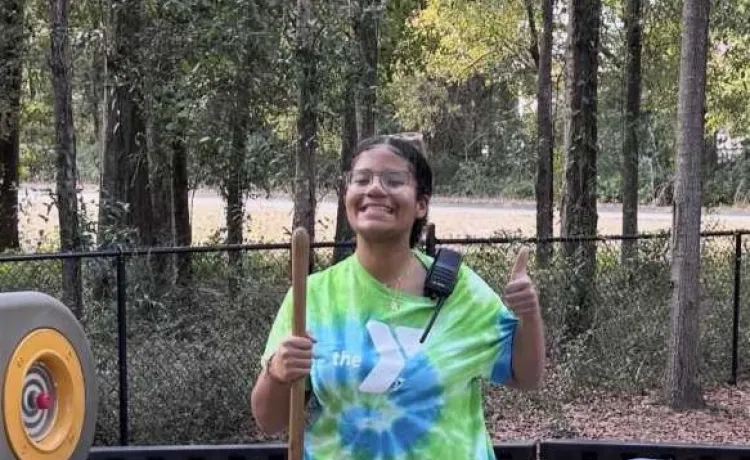 Keiyana poses for a photo with a smile and thumbs up as she helps to spread new mulch on the playground at the Northeast Y.