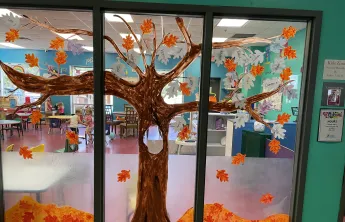 A tree is painted on the windows of KidZone at the Betty J. Pullum Y, with paper leaves decorated by the children.